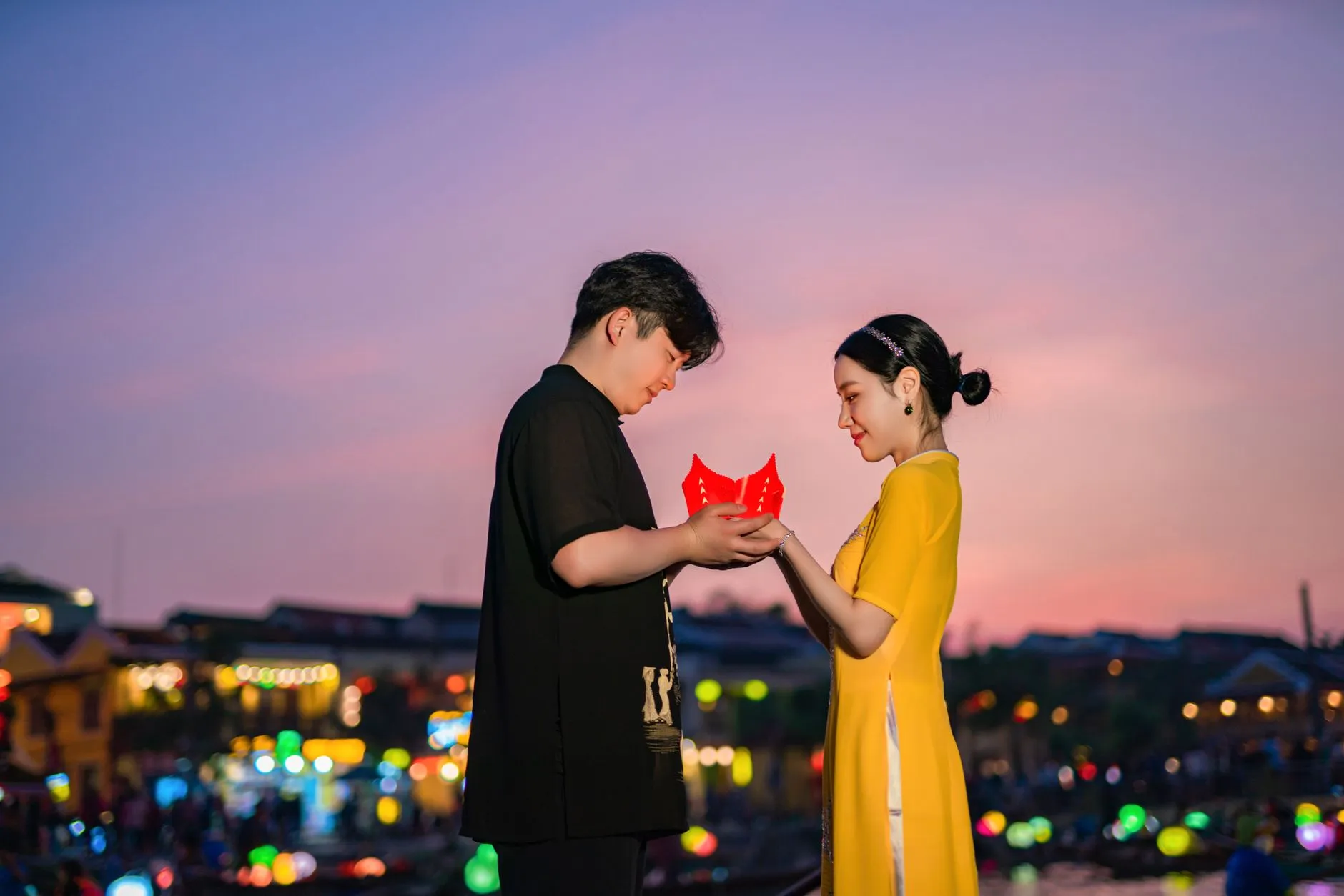 An Asian couple smiling and chatting on a city street in the evening.