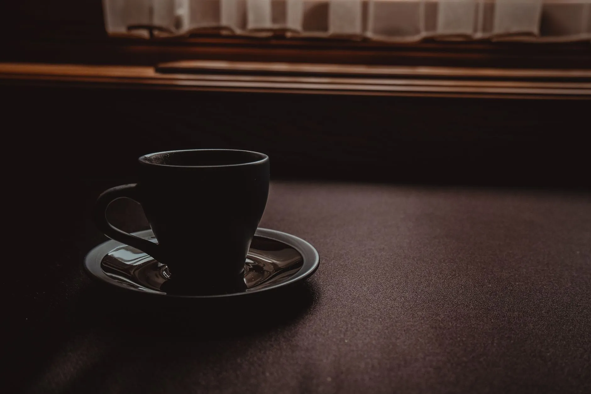 A single coffee cup on a table beside a window in soft, low light.