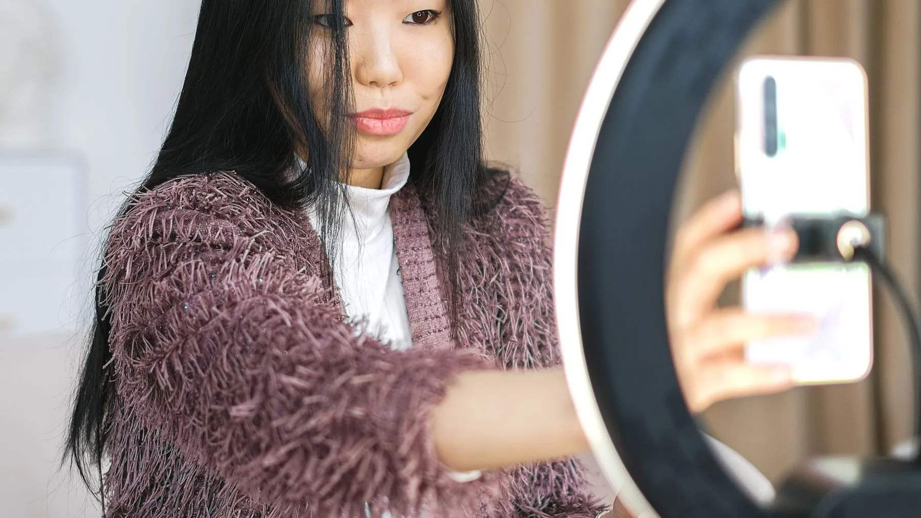 An Asian woman taking a selfie with a smartphone and ring light.