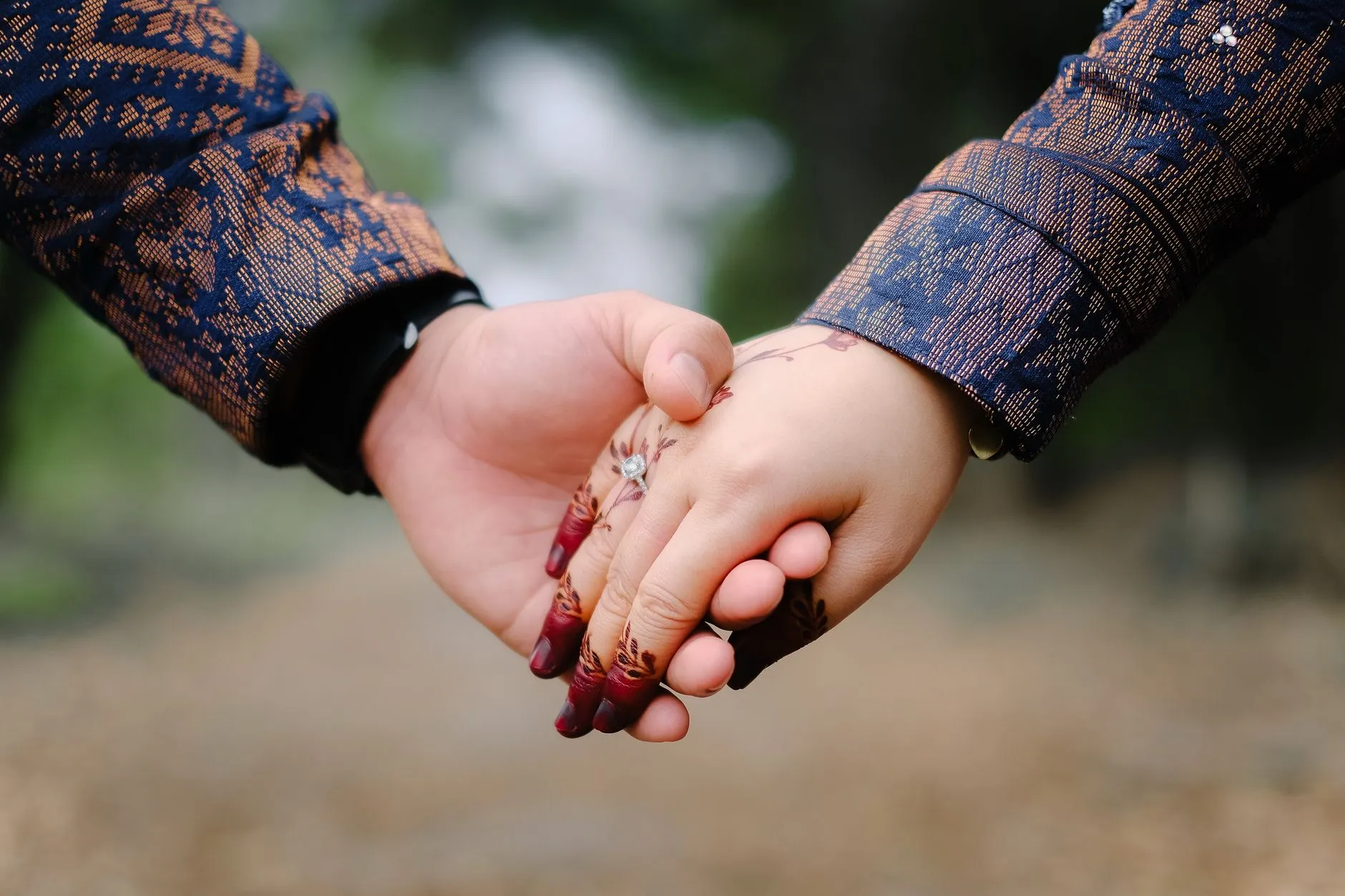 A close-up of two people holding hands outdoors, one hand decorated with henna.