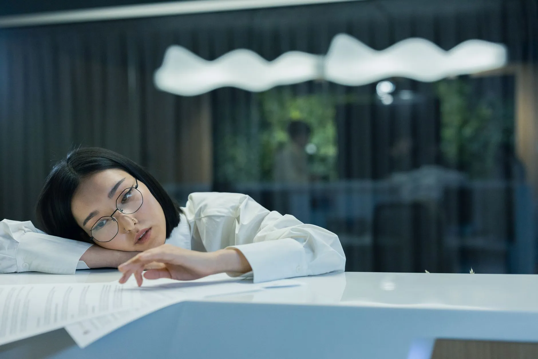 A thoughtful Asian woman reflects while holding her phone at a café table.