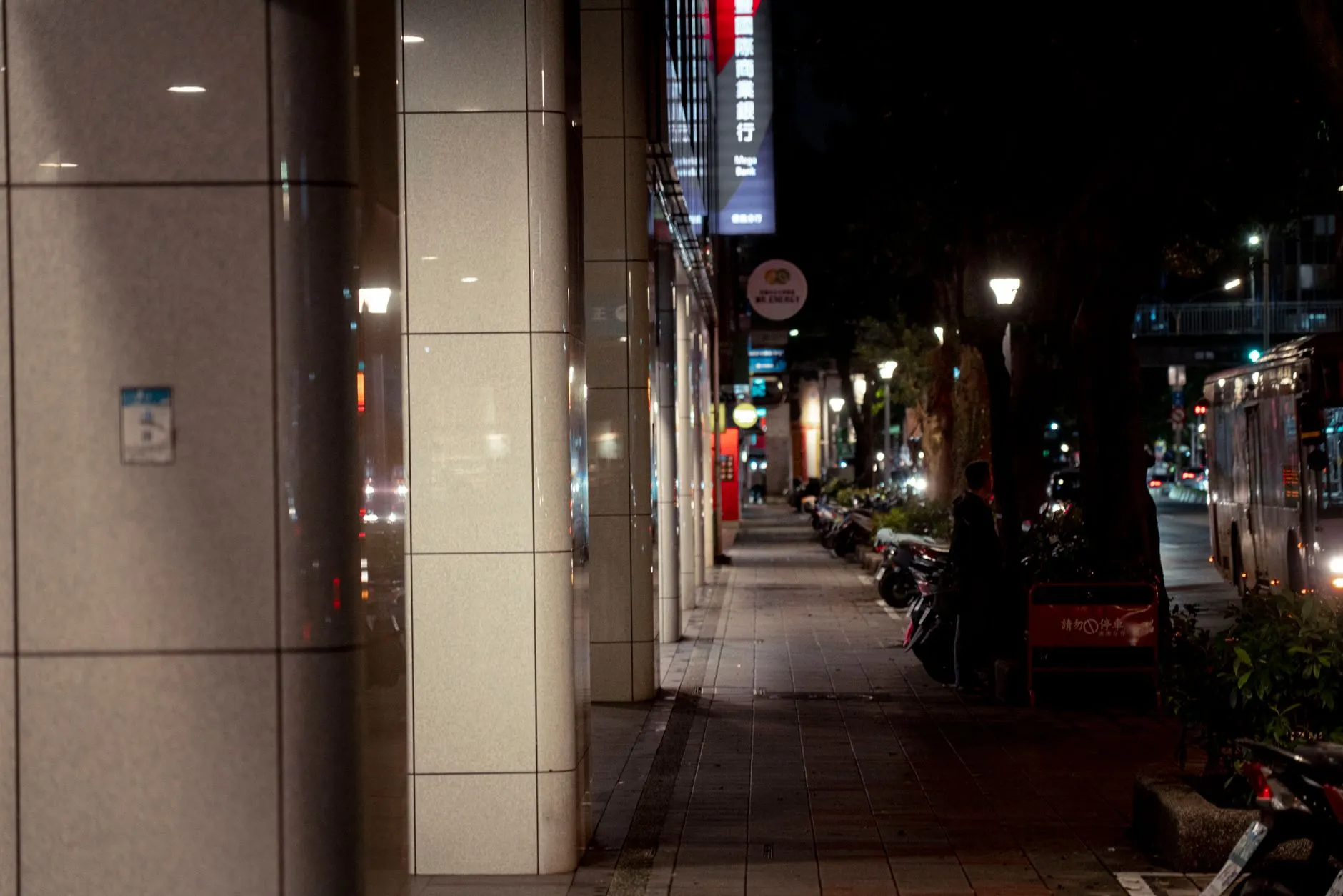 A quiet Taipei street in the evening, lit by shop signs and street lamps.